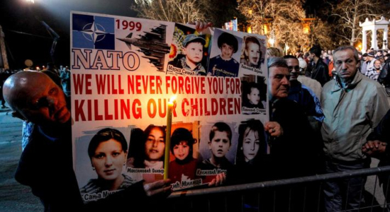 Hombres serbios sostienen un cartel con fotografías de las víctimas de la campaña aérea de la OTAN de 1999 contra Serbia y Montenegro en la ciudad de Nis, el 24 de marzo de 2019 (Foto: AFP) 