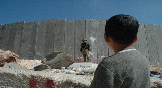 Niño palestino observa a un soldado israelí frente al muro del apartheid. / Imagen de Justin Mcintosh