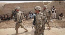  Unos soladaos estadounidenses pasan en frente de los hombres y niños afganos.